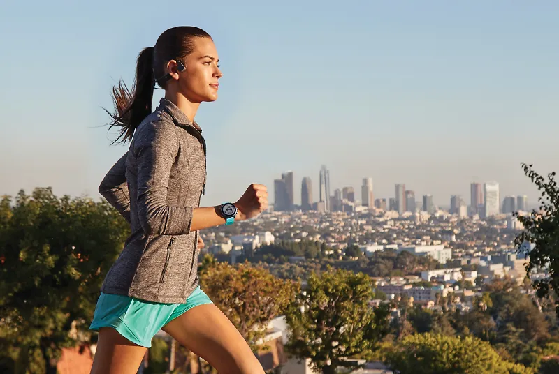 A woman running with headphones and a Garmin watch