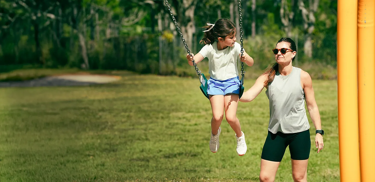 Mother pushes daughter on swing.